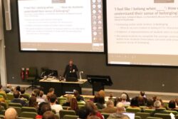 Photo shows Ed Venn, presenter, in lecture theatre with two large screens behind him. 